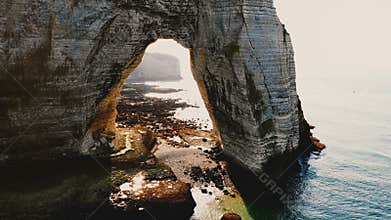 Drone flying through epic natural rocky arch at famous white chalk seaside cliffs at Etretat Normandy on amazing sunset.