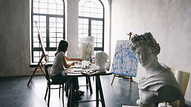 Artist teens girl is working on easel paiting. High contast video footage. Creative workshop filled with sculpture and
