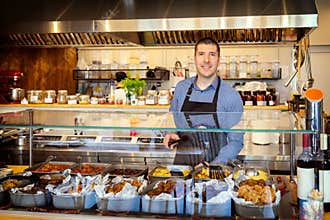 Portrait of smiling owner standing at his eatery serving food behind counter