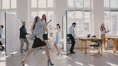 Young happy Caucasian female boss dancing in modern office celebrating together with multiethnic colleagues slow motion.