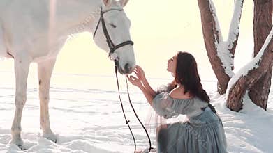 Wonderful warlike girl with black hair sits near magic horse in the snow near the frozen river, lady in a gorgeous gray