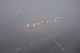 Cars in the fog. Bad winter weather and dangerous automobile traffic on the road. Light vehicles in fog.