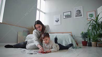 Mother with a child in the white interior of his home to collect the jigsaw puzzle together with his young son. Happy