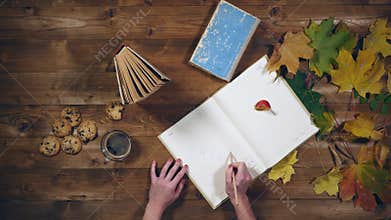 Autumn concept top view. Books, maple leaves, tea on the old wooden table. Woman writing notes in the notebook