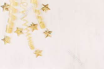 Christmas decorations, curl ribbon and gold stars falling on soft white wooden background.