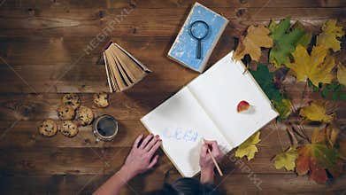 Autumn concept top view. Books, maple leaves, tea on the old wooden table. Woman writing notes in the notebook