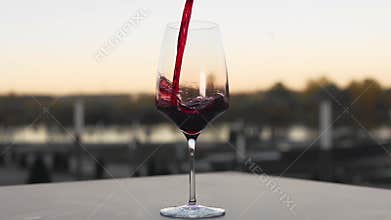 Red wine is poured to the wineglass outdoors in slow motion, bar and restaurant, alcohol drinks, food in slow motion