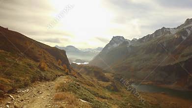 POV walking on fall path to woods, valley lake and snowy mounts at sunset with flare.Sunny autumn day Hiking in colorful