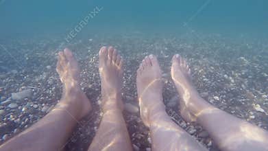 Male and female feet underwater on sea. Couple relaxing at the beach during summer vacation. Point of view POV Close up