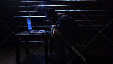 Comic funny hacker commits a cyber attack with a laptop and a gun in his hands