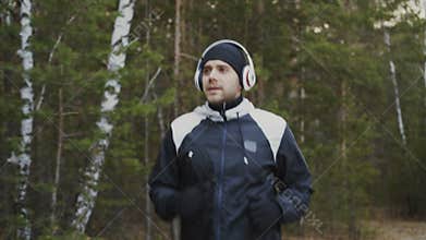 Handsome runner man in headphones jogging while listening music in winter park in the morning