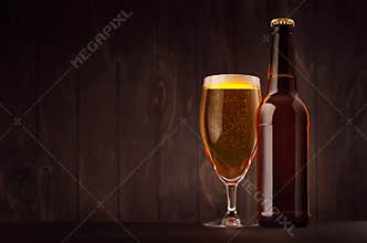 Brown beer bottle and glass tulip with golden lager on dark wood board, copy space, mock up.