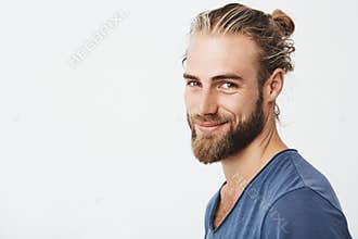 Close up portrait of handsome manly guy with beard posing in three quarters, looking in camera and happily smiling