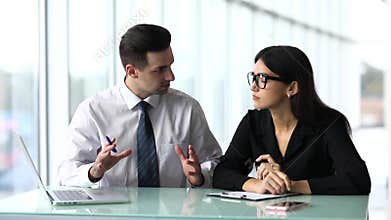 Two happy businesspeople standing in front of office windows, talking and smiling. Team work