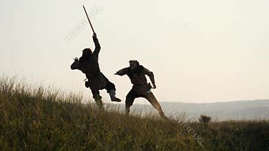 Silhouettes of two warriors Viking are fighting with swords. Contre-jour