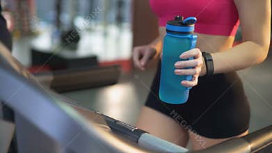 Healthy fit lady exercising on treadmill and drinking water for refreshment