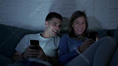 Young happy and romantic couple on their 20s using together mobile phone enjoying sitting at home sofa couch laughing having fun