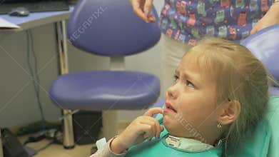 Child with a mother at a dentist`s reception. The girl lies in the chair, behind her mother. The doctor works with an