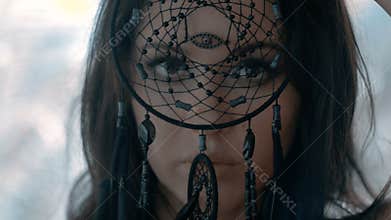 Mysterious woman with make up looking through black dream catcher