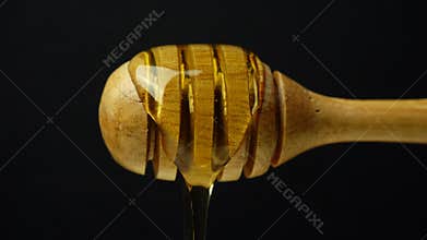 Honey dripping from honey dipper on black background