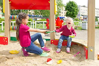Conflict on the playground. Two sisters fighting over a toy shovel in the sandbox