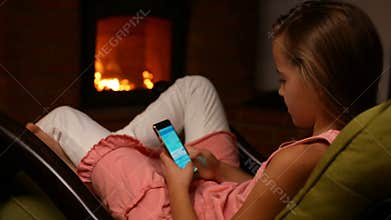 Young girl using her smartphone sitting in a rocking chair