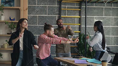 Diverse group female and male start-up business team have fun dancing party in modern office throwing paper documents
