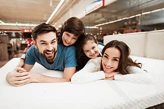 Little children lie on the backs of young happy parents in a mattress store.