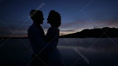 Dark silhouettes of the bride and groom on a tropical ocean beach at sunset. Sensual hugs and kisses.