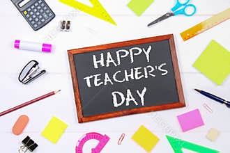 Text chalk on a chalkboard: Happy Teacher`s Day. School supplies, office, books, apple.