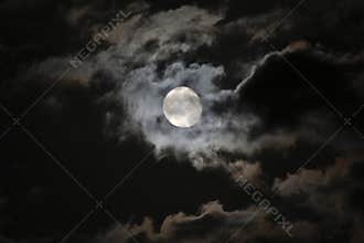 Full moon in eerie white clouds against a black ni