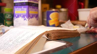 Woman cutting up butter while reading an old cookbook or recipe book in kitchen