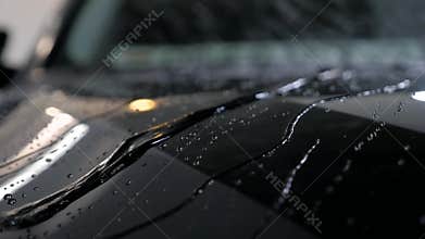 Water drops flow on a black vehicle after car wash