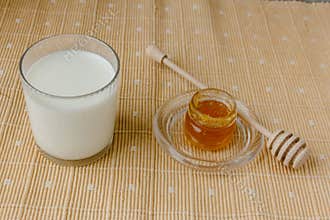 Glass of milk and jar of honey on a textile tablecloth.