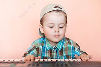 Cute boy wearing baseball cap backwards playing the digital piano