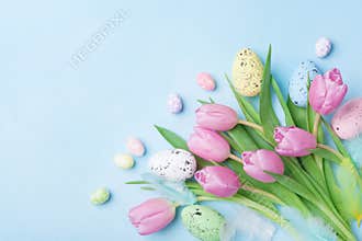 Pink tulip flowers, feathers and colorful eggs on blue table top view. Happy Easter greeting card.