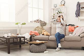 Desperate woman sitting on sofa in messy room