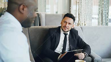 HR businessman having job interview with african american man and watching his resume application in modern cafe