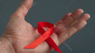 Hand holding red awareness ribbon symbol of HIV AIDS.