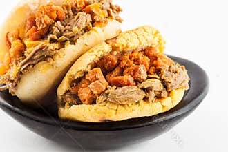 Arepas filled with shredded beef and pork rind served in a black ceramic dish