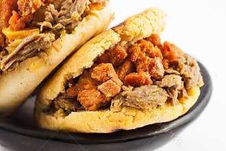 Arepas filled with shredded beef and pork rind served in a black ceramic dish