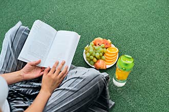 Woman reading book on the lawn, top view over shoulder