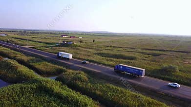 4K AERIAL: Flying high above container semi truck transporting goods on busy highway across the country in beautiful