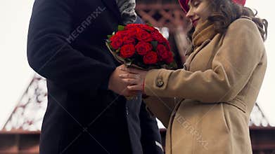Man giving flowers to his beloved and gently hugging her, romance in Paris