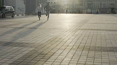 Two amateur runners crossing town square during morning jog, active lifestyle