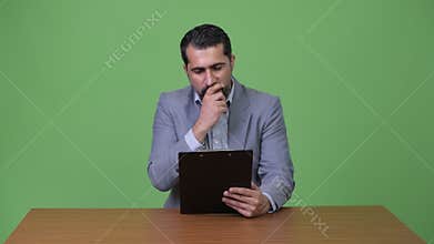 Handsome Persian bearded businessman thinking while holding clipboard