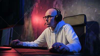 Young man wearing headset and starts online game with his friends. Male gamer smiling and playing online game on a pc