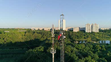 Contractor working on telecommunications mast at height on background of beautiful city landscape, drone view of