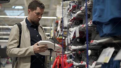 Male shopper is watching pair of sneakers in a sales area in sport store
