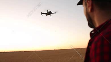 Farmer hands hold remote controller with his hands while quadcopter is flying on background. Drone ascends and flies
